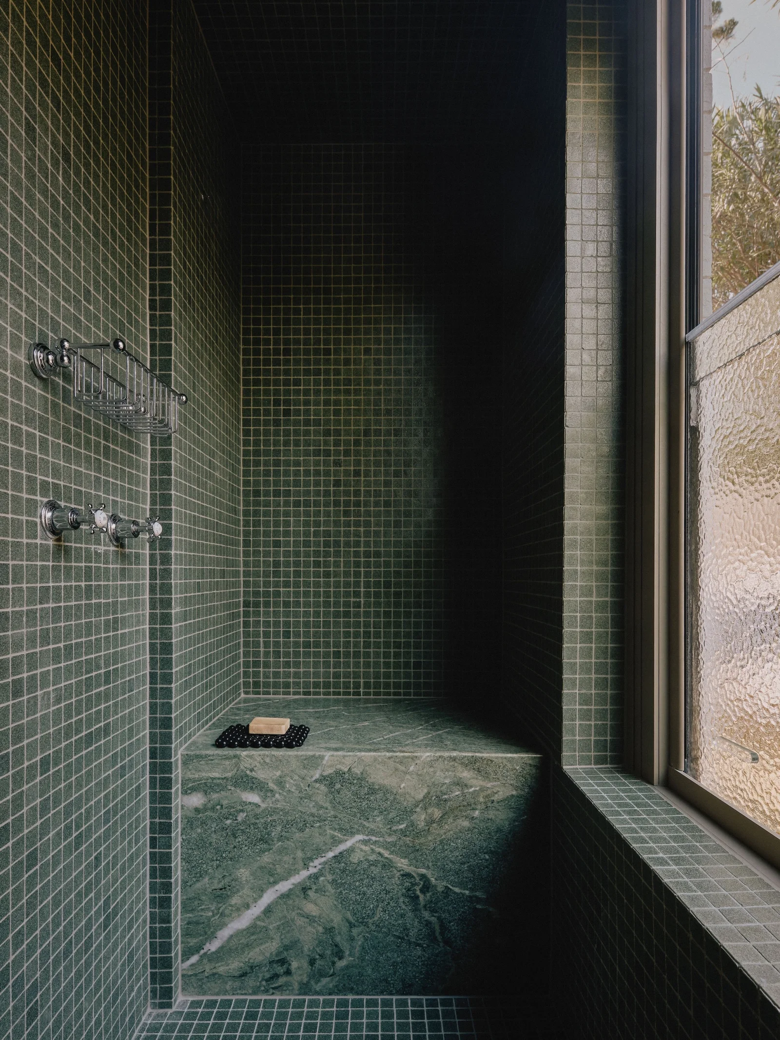 Green marble bench in a dark green mosaic tiled shower