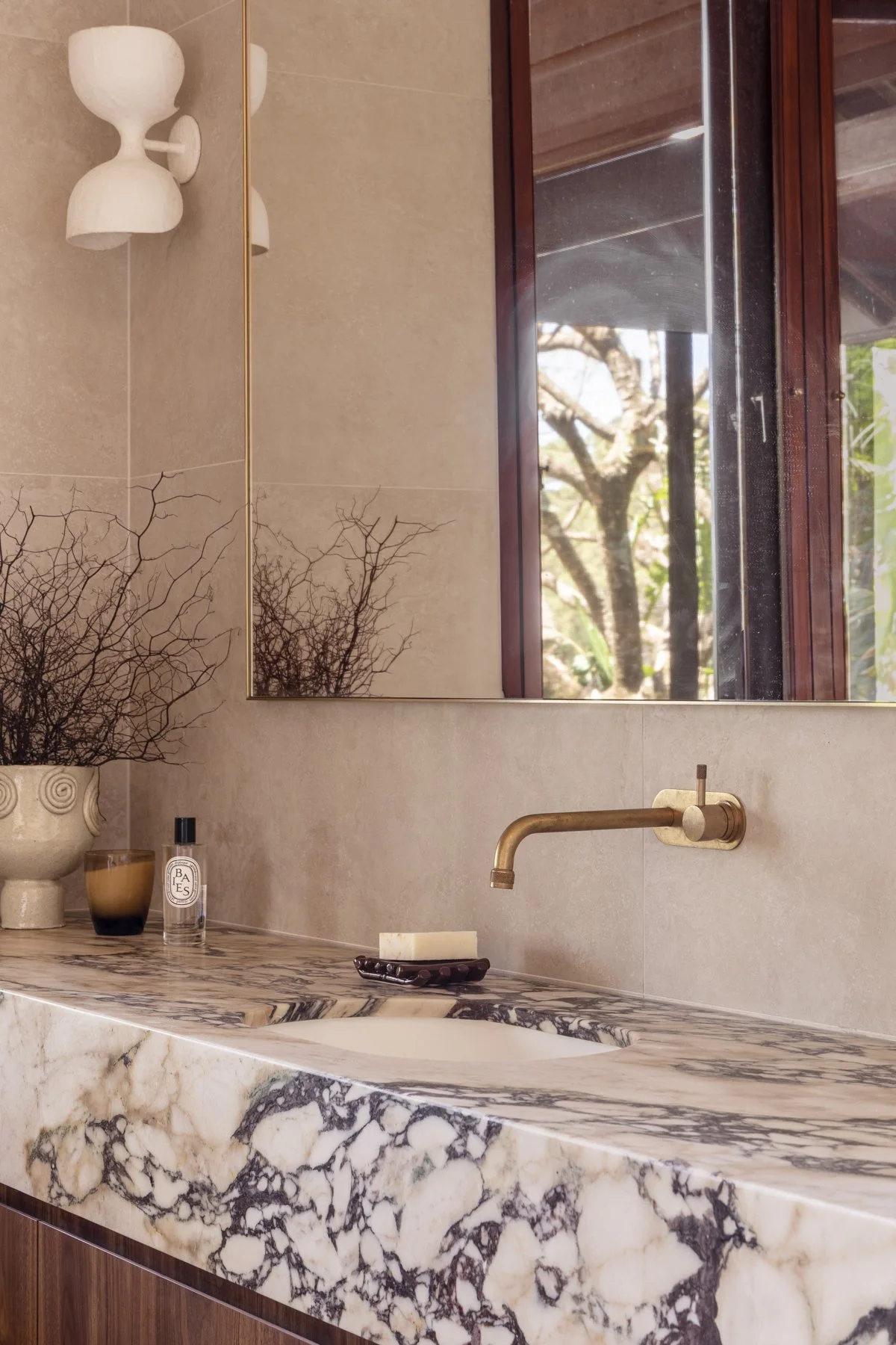 Veined marble vanity top floating on a walnut cabinet with a brass tap