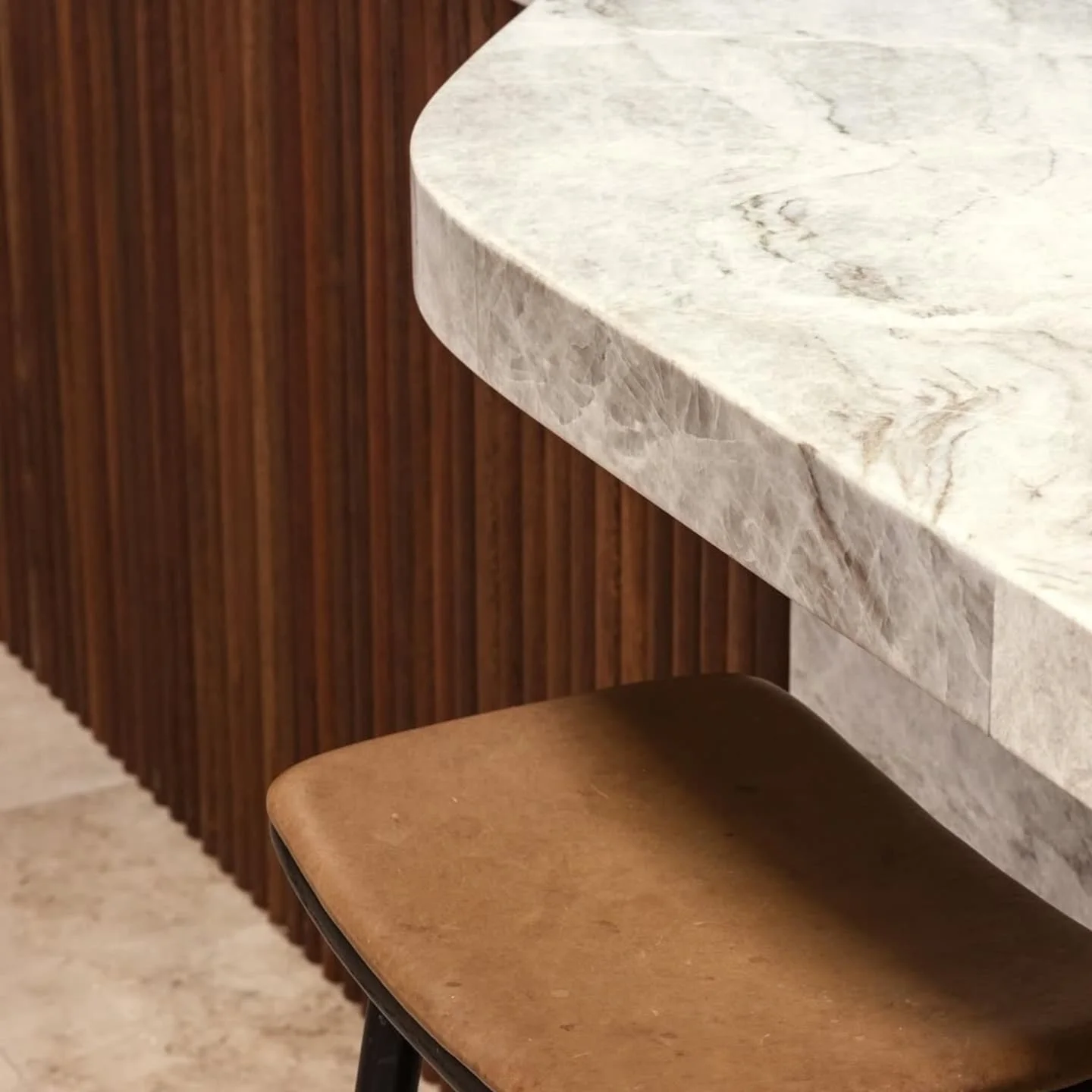 Curved quartzite benchtop edge above fluted timber and a leather stool