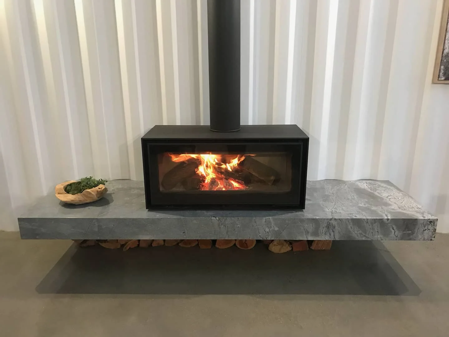 Black wood heater on a solid stone hearth in front of a white curtain