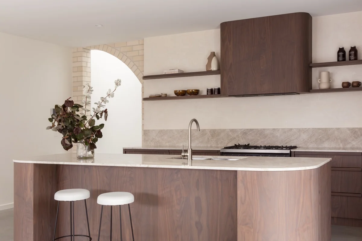 Walnut kitchen island with a Taj Mahal quartzite benchtop under a brick arch