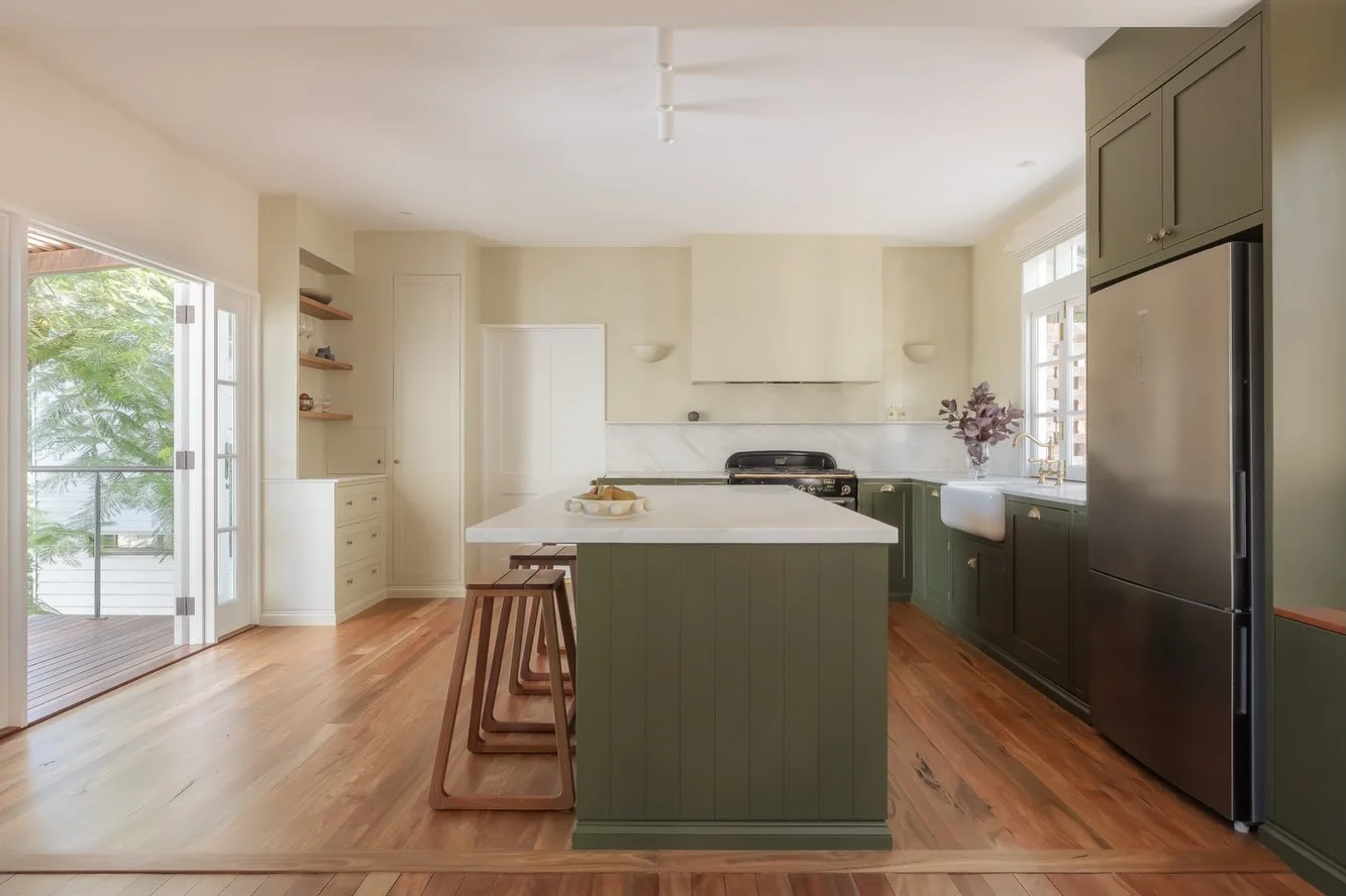 Marble topped green island with timber stools in a white kitchen