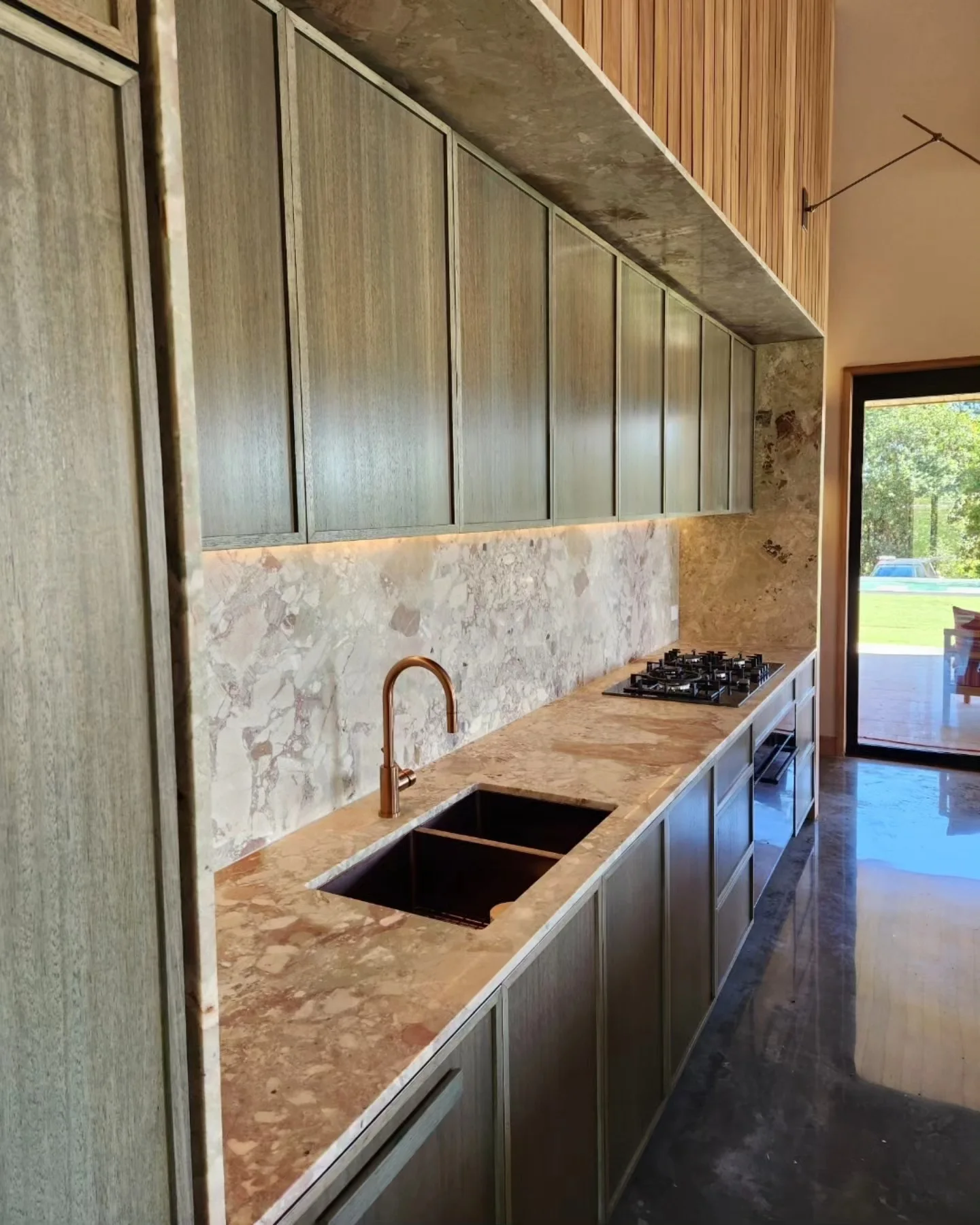 Veined stone splashback and benchtop with green cabinets and a brass tap
