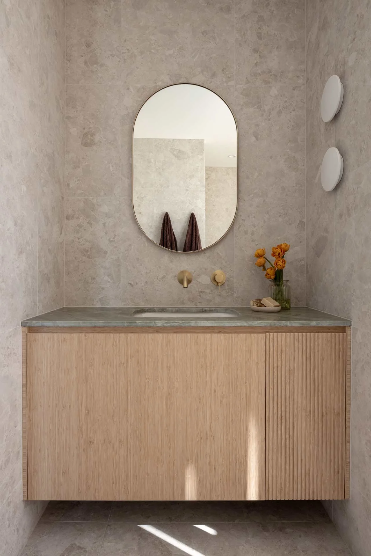Two oval mirrors above a timber vanity with a stone top and a herringbone stone wall